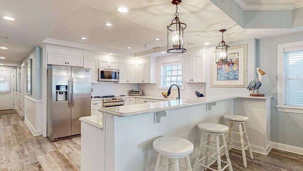 A modern kitchen with white cabinets, stainless steel appliances, and a central island with stools. - Sunny - Ocean Block Condo, steps to the beach with pool, balcony & fitness room (Ocean City)