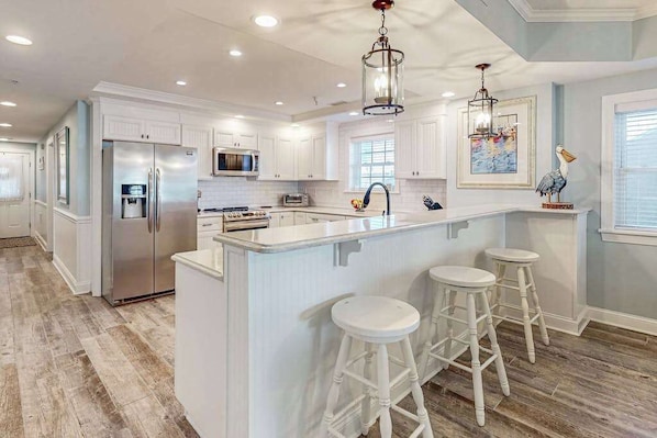A modern kitchen with white cabinets, stainless steel appliances, and a central island with stools. - Sunny - Ocean Block Condo, steps to the beach with pool, balcony & fitness room (Ocean City)