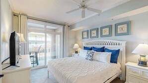 A bedroom with a bed, two bedside tables with lamps, a ceiling fan, and a large window. - Sunny - Ocean Block Condo, steps to the beach with pool, balcony & fitness room (Ocean City)