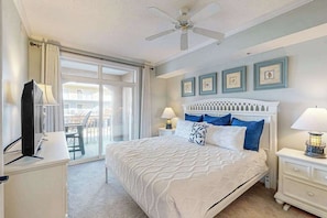 A bedroom with a bed, two bedside tables with lamps, a ceiling fan, and a large window. - Sunny - Ocean Block Condo, steps to the beach with pool, balcony & fitness room (Ocean City)