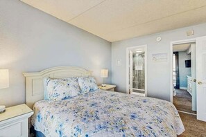 A bedroom with a bed, nightstand, and a door leading to a bathroom. - Beach condo with balcony, indoor/outdoor pools, game room & gym (Ocean City)