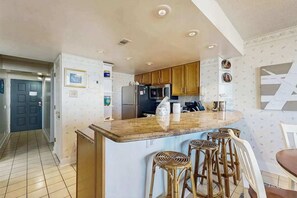 A kitchen with a central island, wooden cabinets, and a dining area with stools. - Beach condo with balcony, indoor/outdoor pools, game room & gym (Ocean City)