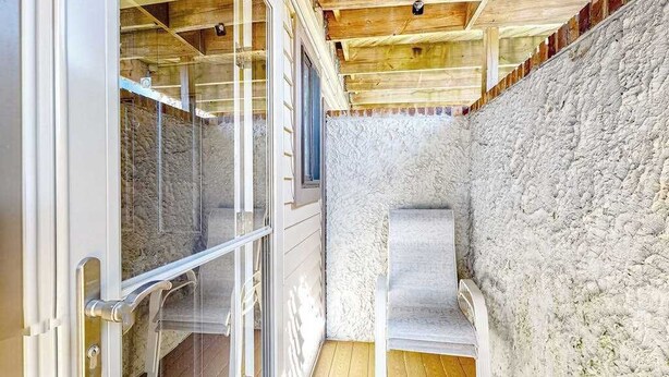 Een kamer met een stenen muur, houten plafond en een glazen deur naar een balkon.