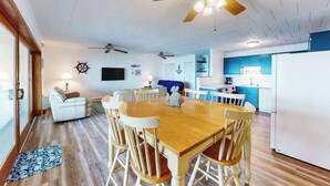 A dining area with a wooden table and chairs, a ceiling fan, and a kitchen with blue cabinets. - Calypso 406 (Ocean City)