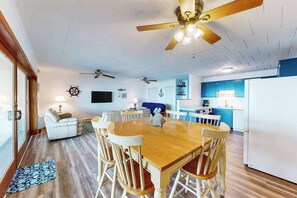 A dining area with a wooden table and chairs, a ceiling fan, and a kitchen with blue cabinets. - Oceanfront condo with balcony, pool, washer/dryer, & full kitchen - golf nearby (Ocean City)
