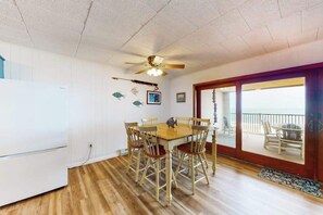 Comedor con mesa y sillas de madera, ventilador de techo y vista al exterior por un ventanal.