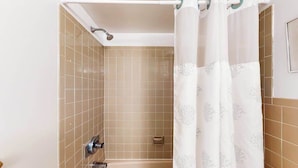 A bathroom with beige tiled walls, a bathtub, a shower with a curtain, and a toilet. - Calypso 406 (Ocean City)