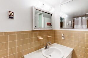 Un baño con lavamanos blanco, espejo y una lámpara fijada a la pared.