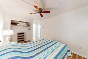 Un dormitorio con cama, ventilador de techo, armario y puerta que da a otra habitación.
