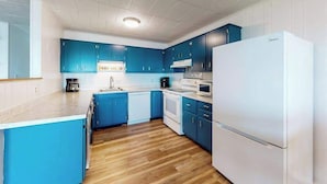 A modern kitchen with blue cabinets, a white refrigerator, and a wooden floor. - Calypso 406 (Ocean City)