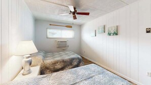 A bedroom with two beds, a ceiling fan, a window with blinds, and wall-mounted artwork. - Calypso 406 (Ocean City)