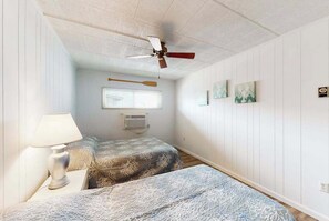A bedroom with two beds, a ceiling fan, a window with blinds, and wall-mounted artwork. - Oceanfront condo with balcony, pool, washer/dryer, & full kitchen - golf nearby (Ocean City)