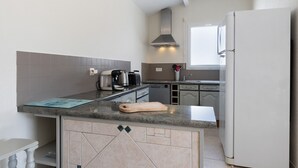 Una cocina con encimera de granito, campana extractora de acero inoxidable, refrigerador blanco y una ventana que proporciona luz natural.