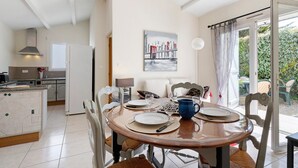 Comedor con una mesa redonda para cuatro, cocina al fondo y vista al exterior a través de un ventanal.