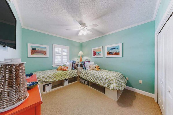 Een slaapkamer met twee bedden, een plafondventilator en kunstwerken aan de muur.