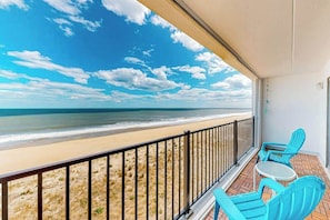 A balcony with a view of the beach, a railing, and two blue chairs. - Beachfront condo with ocean views, private balcony, central AC, & W/D (Ocean City)