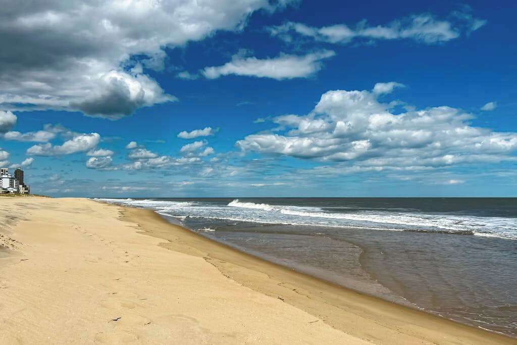 Une plage avec un ciel dégagé, des vagues et un bâtiment situé sur la gauche.