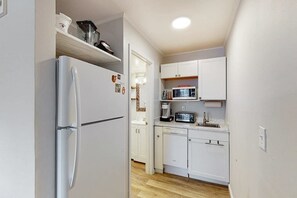 Eine kleine Küche mit weißen Schränken, einer eingebauten Mikrowelle und einem Kühlschrank.