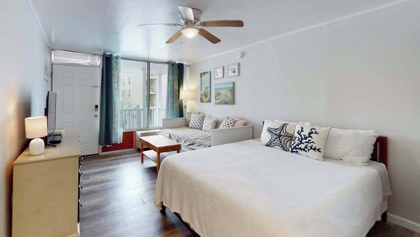 A bedroom with a bed, a desk, a chair, a ceiling fan, and a door leading to a balcony. - Ocean Waye 226 (Ocean City)