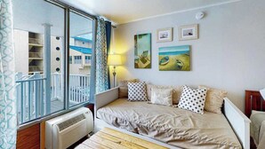 A bedroom with a large window, a bed with patterned pillows, a wall-mounted lamp, and a view of a building outside. - Ocean Waye 226 (Ocean City)