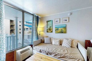 Ein Schlafzimmer mit großem Fenster, einem Bett mit gemusterten Kissen, einer Wandleuchte und Blick auf ein Gebäude.