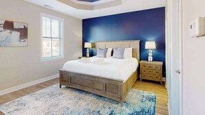 Une chambre à coucher avec un lit, des tables de chevet, un ventilateur de plafond, une fenêtre et un tableau au mur.