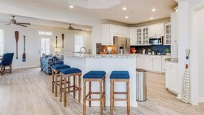 Une cuisine spacieuse avec des meubles blancs, un îlot central doté de tabourets et un ventilateur de plafond.