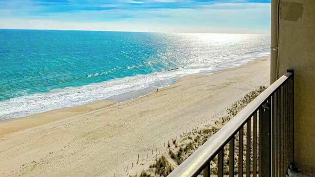 Une vue sur la plage depuis un balcon doté d’une balustrade, avec une plage de sable et l’océan en toile de fond.