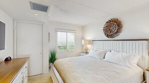 Ein Schlafzimmer mit Bett, Nachttisch, Lampe, Wanddekoration, Fenster und Tür.