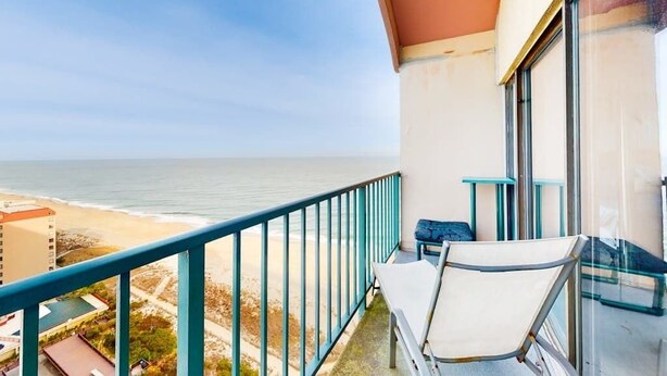 Un balcon avec vue sur la plage et l’océan, une chaise et une petite table.