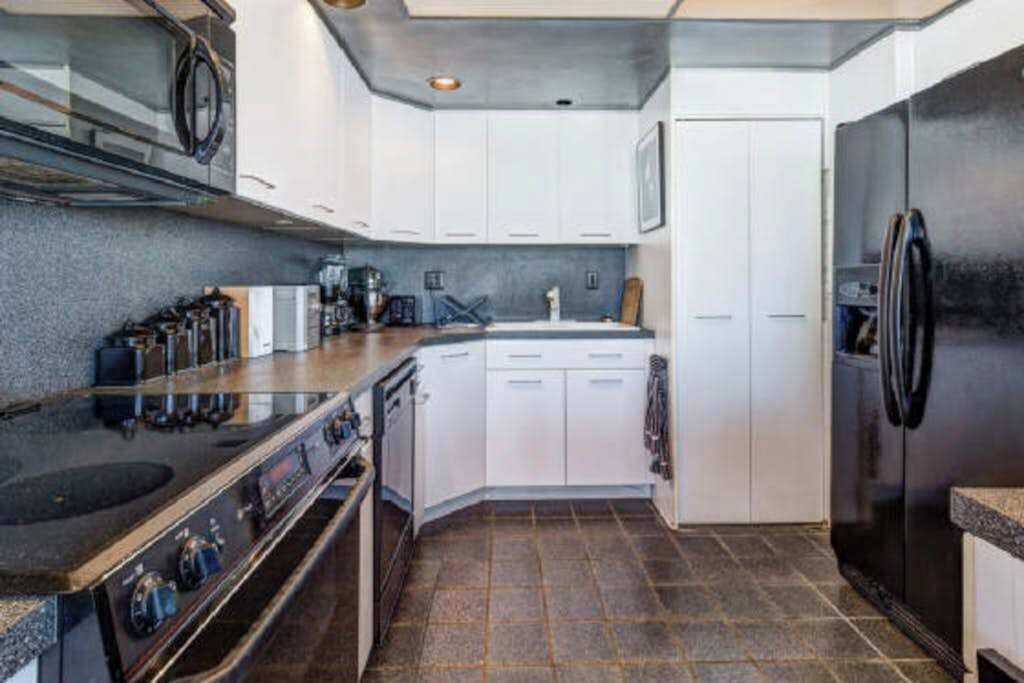 A modern kitchen with a stove, oven, refrigerator, and white cabinets.