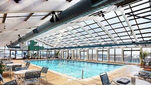 Une piscine intérieure dotée d’un toit en verre, de chaises longues et de tables.