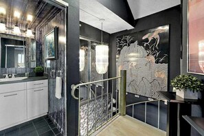 A modern bathroom with a large mirror, a chandelier, and a decorative wall piece. - 20th-floor beachfront condo with ocean views, indoor/outdoor pools, & gym (Ocean City)