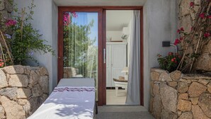 Un dormitorio con cama, pared de piedra y vista a otra habitación con una silla y una lámpara.