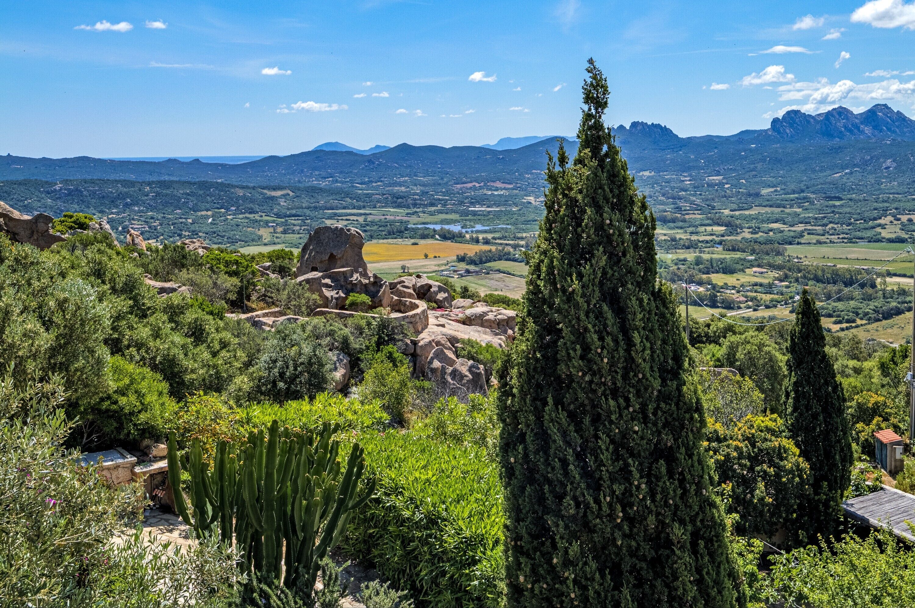 A mountainous landscape with a clear sky, rocky terrain, and dense vegetation.