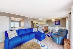 Ein Wohnzimmer mit einem blauen Sofa, einem blauen Sessel und einem Essbereich mit weißen Stühlen.