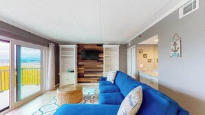 Un salon avec un canapé bleu, un téléviseur à écran plat, un panneau mural en bois et une vue à travers une porte-fenêtre coulissante.