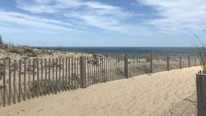 Une plage de sable avec une clôture en bois et un ciel dégagé.