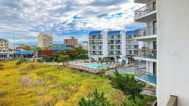 Un hôtel à plusieurs étages doté d’une piscine sur le toit, entouré d’espaces verts et d’autres bâtiments.