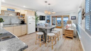 A modern kitchen with a central island, bar stools, and a view of the ocean. - Beachcrest 14 (Ocean City)
