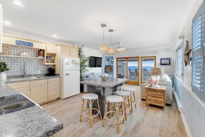 A modern kitchen with a central island, bar stools, and a view of the ocean. - Beachcrest 14 (Ocean City)