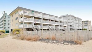 A multi-story residential building with balconies, a sandy beach in front, and a clear sky. - Beachcrest 14 (Ocean City)