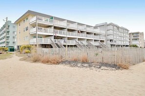A multi-story residential building with balconies, a sandy beach in front, and a clear sky. - Beachcrest 14 (Ocean City)