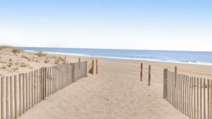 A sandy beach with a wooden fence and rope barrier leading to the ocean. - Beachcrest 14 (Ocean City)