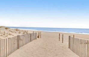 A sandy beach with a wooden fence and rope barrier leading to the ocean. - Beachcrest 14 (Ocean City)