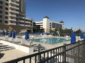 A hotel pool area with sun loungers and umbrellas, a parking garage, and a multi-story building with balconies. - 14 Clipper on the Bay (Ocean Pines)