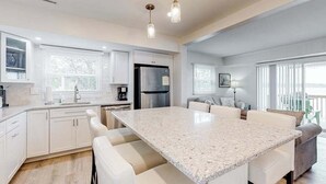 Une cuisine moderne avec des meubles blancs, un îlot en granit et des luminaires suspendus.