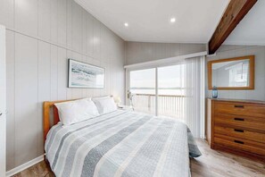 A bedroom with a bed, a dresser, a large window with curtains, a framed picture on the wall, and a wooden ceiling beam. - 14 Clipper on the Bay (Ocean Pines)