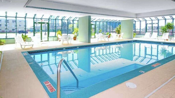An indoor swimming pool with clear glass walls, lounge chairs, and potted plants. - Makai 403 (Ocean City)