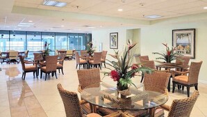 A spacious indoor area with multiple wicker chairs and tables, a glass coffee table, and potted plants. - Makai 403 (Ocean City)